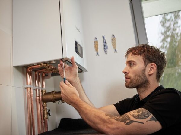 A heating engineer using a screwdriver to work on the pipework beneath a wall-mounted Vaillant boiler