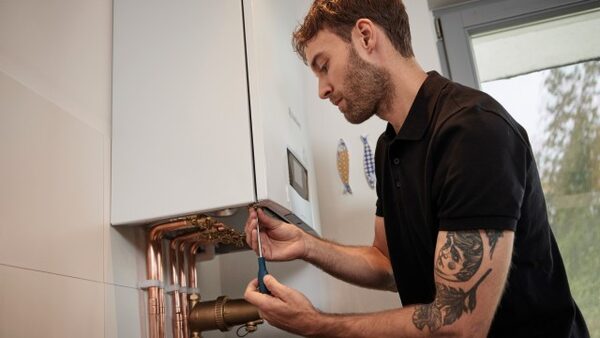 An engineer using a screwdriver on the copper pipework beneath a wall-mounted Vaillant ecoTEC plus boiler in a home