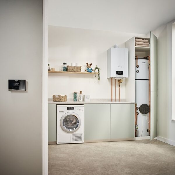 A Vaillant wall-mounted boiler and a hot water cylinder installed in a utility room with a washing machine and a wall thermostat