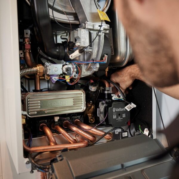 A technician working inside the open casing of a Vaillant combi boiler, with copper pipework and internal components visible