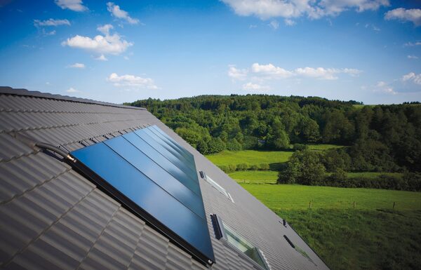 Flat-plate solar thermal collector panels installed on a grey tiled roof overlooking green countryside