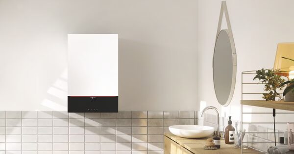 A white Viessmann wall-mounted gas combi boiler installed on a tiled bathroom wall above a wooden vanity with a basin and mirror
