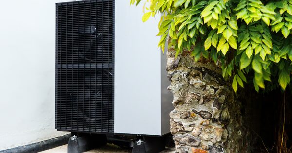 A Viessmann air source heat pump unit installed outside against a white wall beside a stone pillar and green foliage