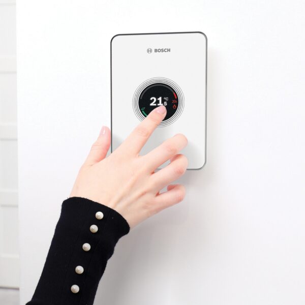 A hand adjusting a white Bosch EasyControl smart thermostat on a wall, showing 21.5°C