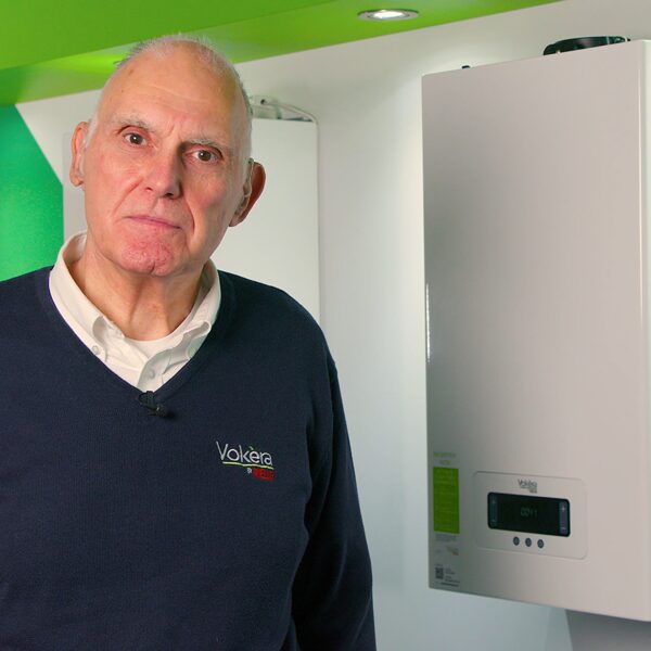 A man in a Vokera-branded jumper standing next to a wall-mounted Vokera boiler