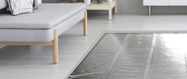 A Warmup electric underfloor heating mat laid on a floor next to a grey sofa in a modern living room