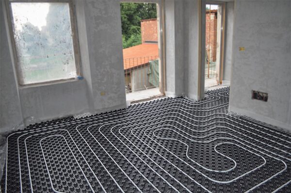 Hydronic underfloor heating pipes laid in loops on black studded panels in an unfinished room