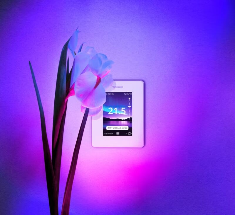 A Warmup smart thermostat displaying 21.5°C on a vivid purple and pink background with a white orchid flower in front