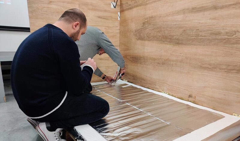 Two installers fitting Warmup foil underfloor heating mats on a floor in a training room