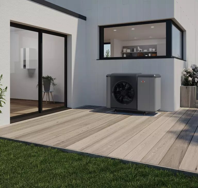 A WOLF air source heat pump unit installed on a wooden terrace outside a modern white house