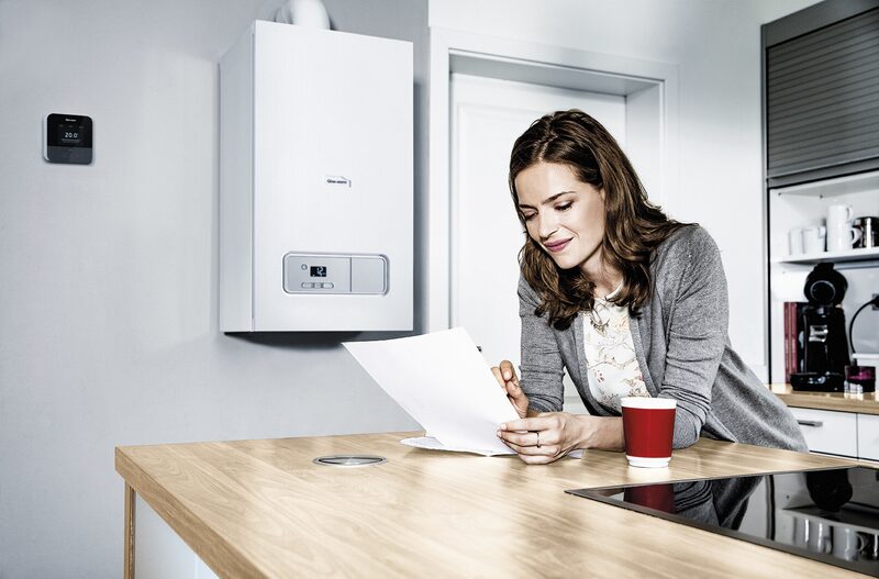 A woman reading a document at a kitchen counter with a wall-mounted Vaillant combi boiler and smart thermostat behind her