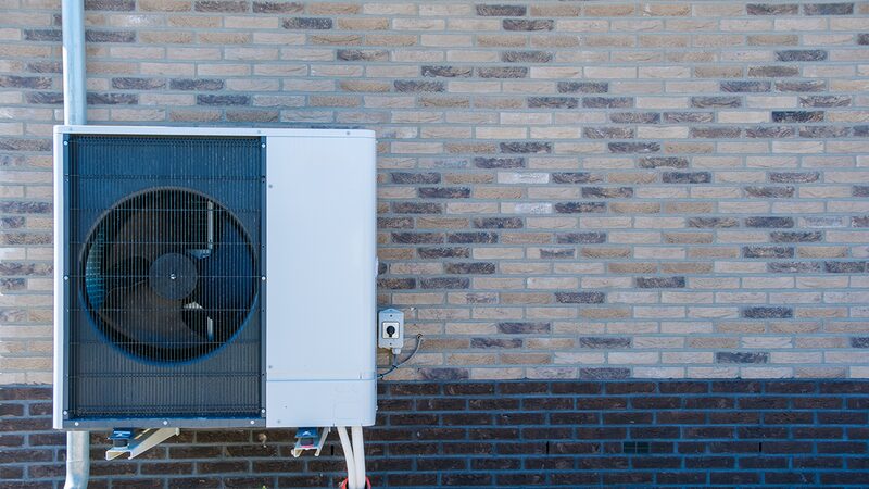 An air source heat pump unit mounted on the exterior brick wall of a building