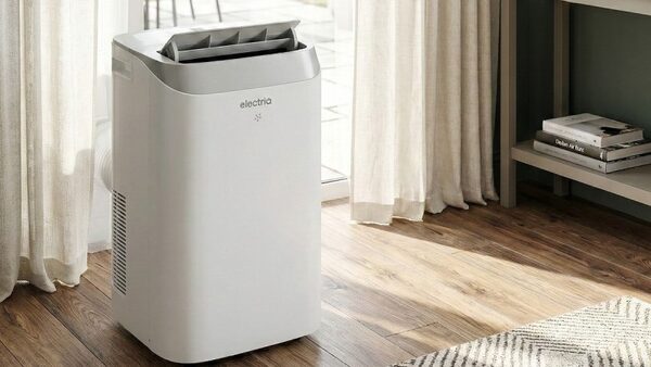 A white electriQ portable air conditioner standing in a bright room with wooden flooring and curtains