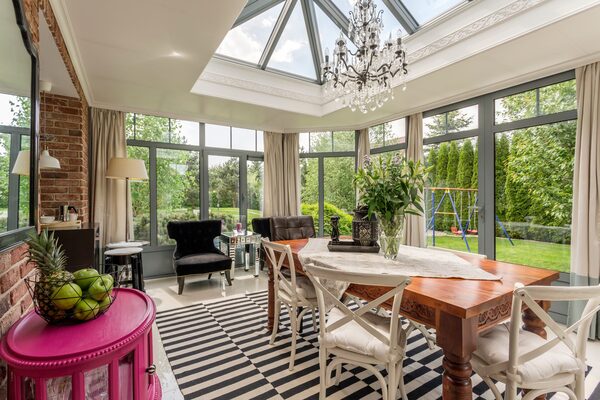 A bright conservatory interior with a glazed roof lantern, large windows, a dining table and seating