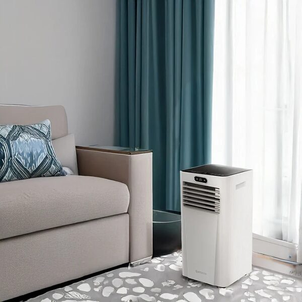 A white Meaco portable air conditioner standing in a living room beside a sofa and curtains