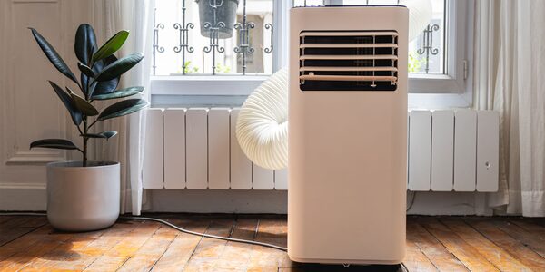 A portable air conditioner with an exhaust hose in a bright room next to a radiator and potted plant
