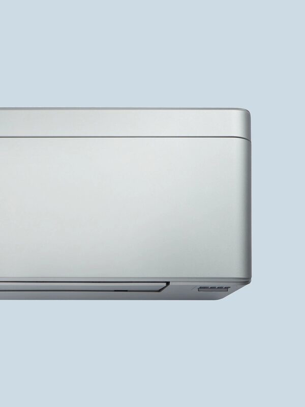 A close-up of a white wall-mounted air conditioning indoor unit against a pale blue background
