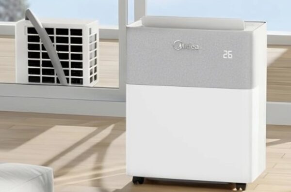 A Midea portable split air conditioner unit standing on a wooden floor next to a window with the outdoor unit visible outside