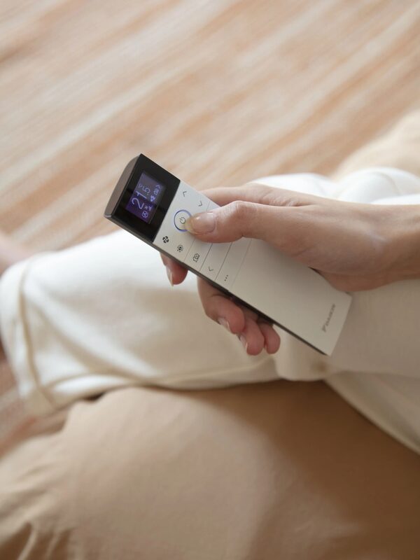 A close-up of a hand holding a white Daikin heat pump remote control displaying a temperature setting