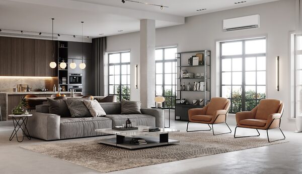 A wall-mounted white air conditioning unit installed high on the wall of a modern open-plan living room with sofas and armchairs