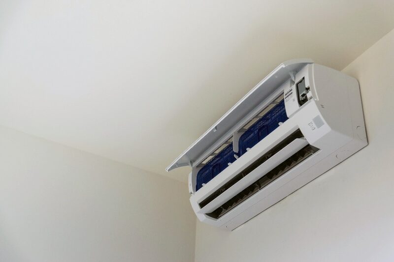 A white wall-mounted split air conditioning indoor unit with its front panel open, installed high on a plain wall