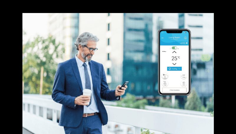 A man in a suit using a smartphone next to an enlarged phone screen showing the Hitachi airHome app controlling a Living Room air conditioner at 25°C