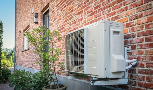 An air-to-air heat pump outdoor unit mounted on the brick exterior wall of a house