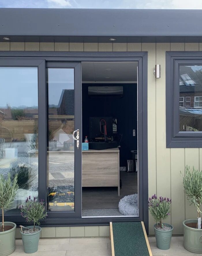 A wall-mounted air conditioning unit installed inside a garden room, seen through open sliding doors of the building exterior