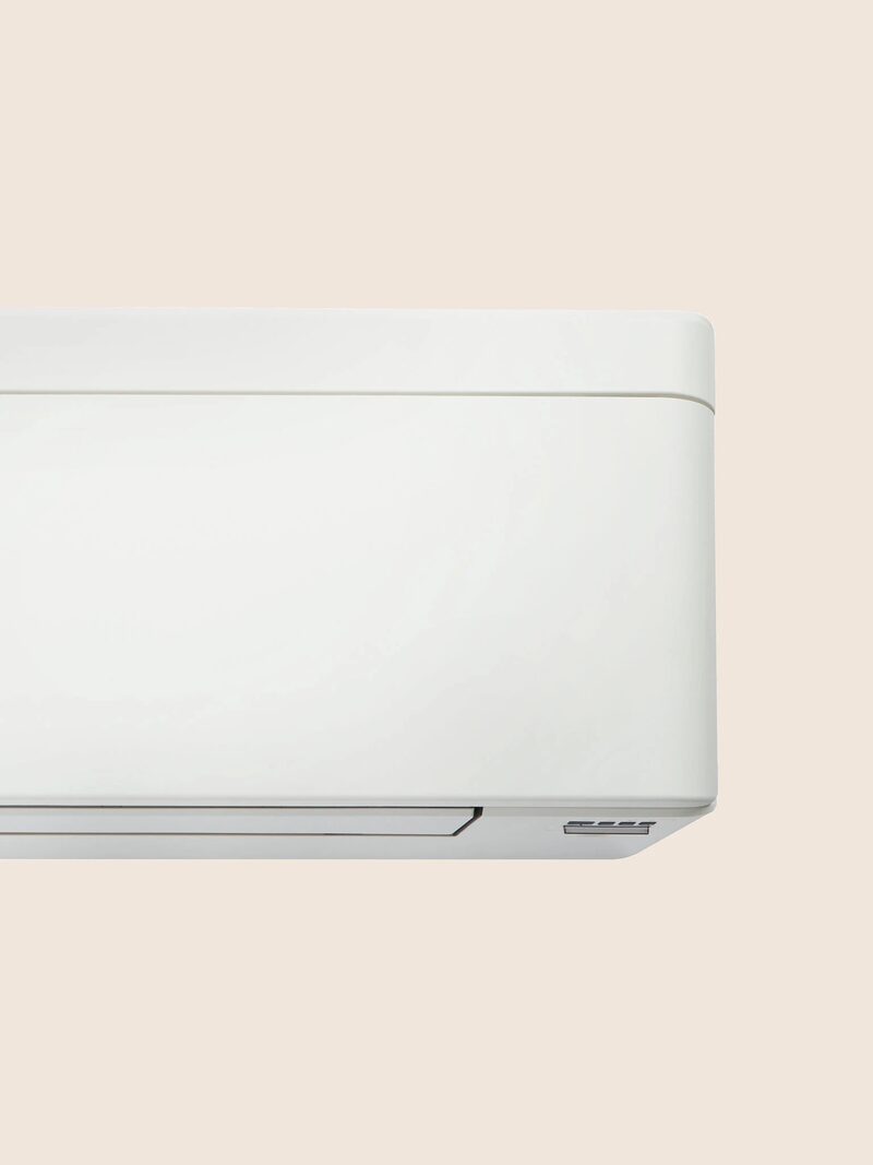 A close-up of a white wall-mounted air conditioning indoor unit against a plain beige background