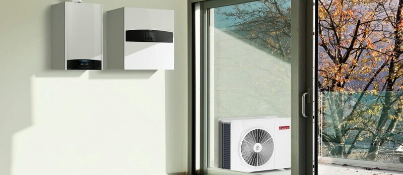 A wall-mounted boiler and heat pump indoor unit inside a home with an outdoor heat pump unit visible through a glass door