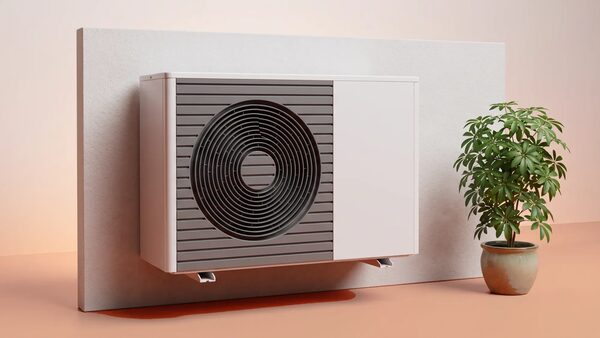 A white wall-mounted air-to-air heat pump unit on a plain wall next to a potted plant
