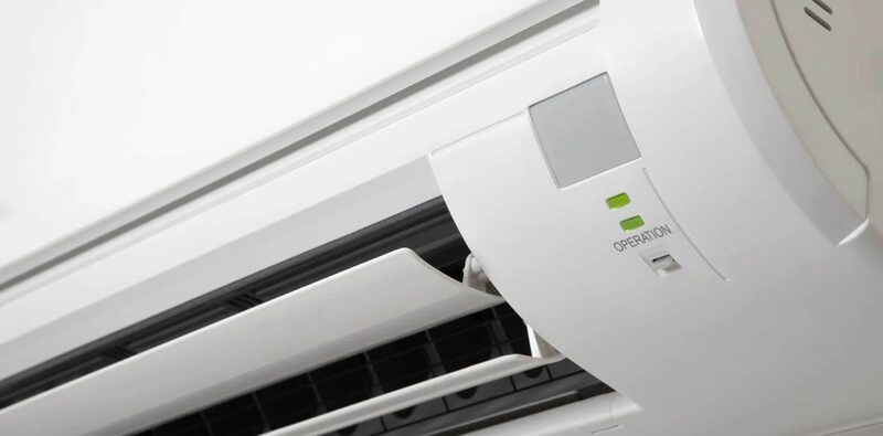 A close-up of a white wall-mounted air conditioning unit with its operation indicator lights lit
