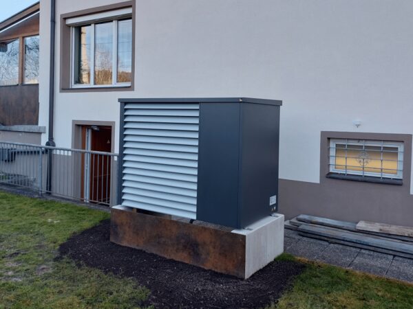 An outdoor air-source heat pump unit with louvred side panels installed on a concrete plinth against the wall of a house