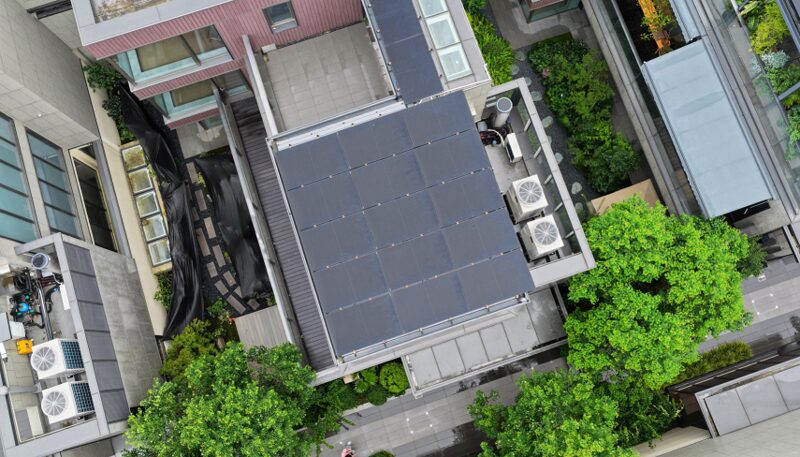 Aerial view of a rooftop solar panel array on a modern building surrounded by trees and air conditioning units