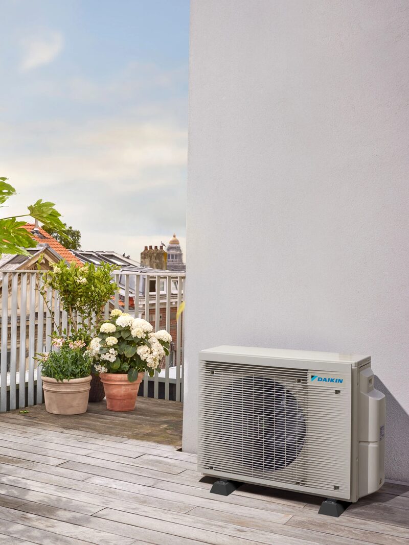 A Daikin air conditioning outdoor unit installed on a wooden terrace beside a white wall with potted plants