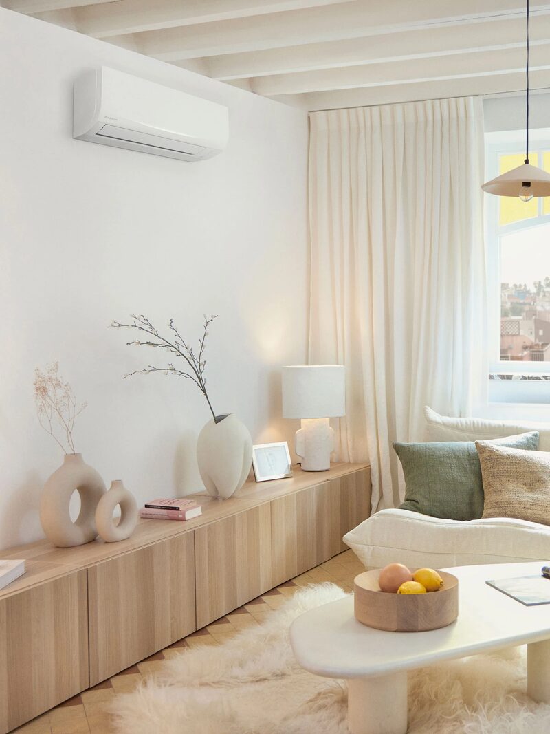 A white wall-mounted Daikin air conditioning unit installed high on the wall of a bright, neutrally decorated living room