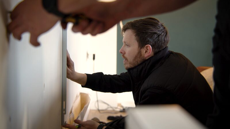 An installer fitting an indoor unit of an air-to-air heat pump to a wall inside a home