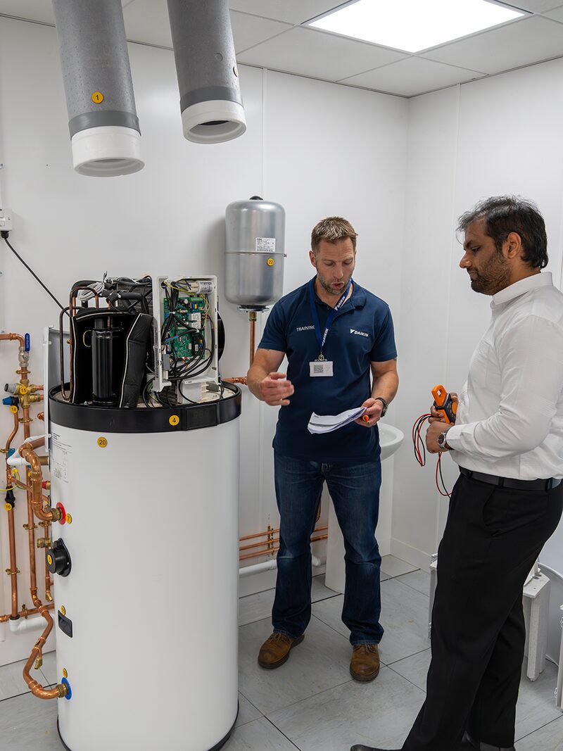 A Daikin trainer explaining a heat pump cylinder installation to a trainee in a training room