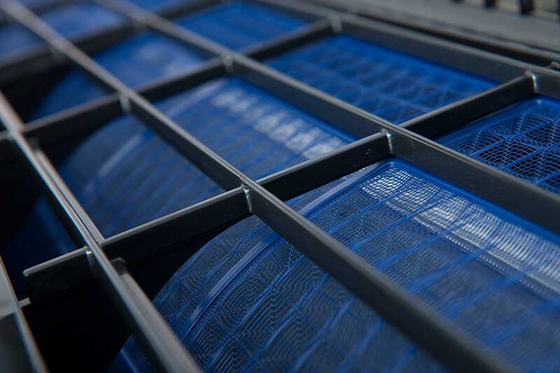 Close-up of blue filters behind a dark metal grille inside an air conditioning or ventilation unit