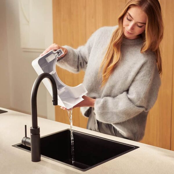 A woman emptying the water tank of a Duux Bora dehumidifier into a kitchen sink