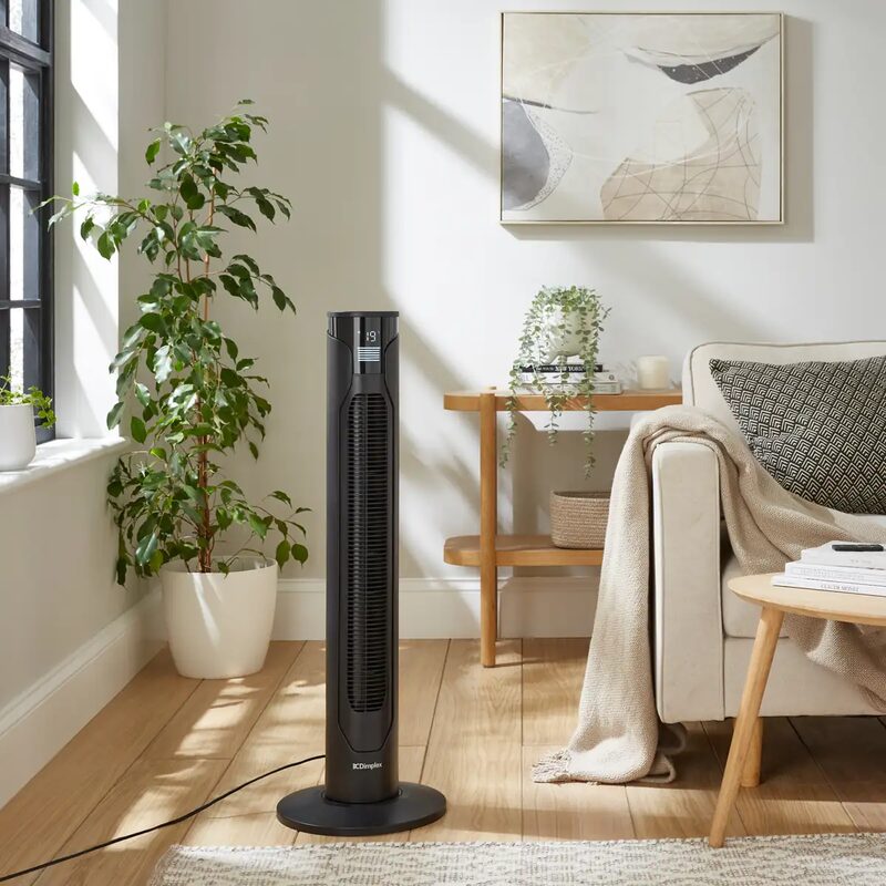 A black Dimplex tower fan standing in a bright living room beside a sofa and houseplants