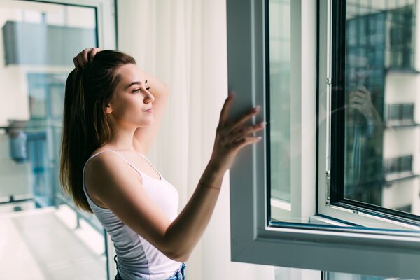 A young woman opening a large white-framed window in a modern apartment