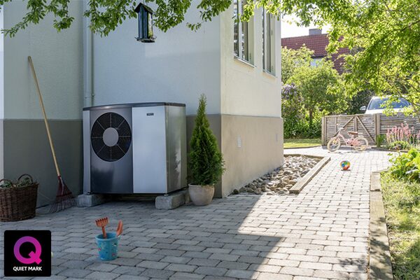 An air source heat pump unit installed outside a house on a block-paved garden path