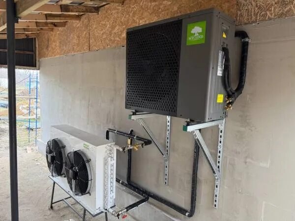 A Mycond split heat pump outdoor unit and fan unit installed on an unfinished exterior wall with pipework