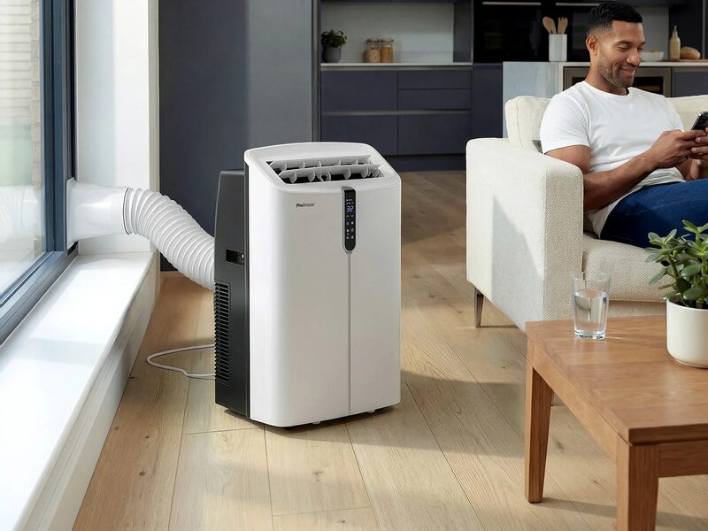 A white Pro Breeze portable air conditioner vented through a window hose in a living room with a man on a sofa