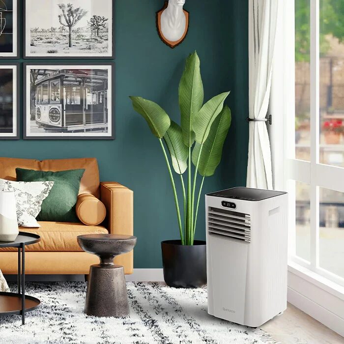 A white Meaco portable air conditioner standing in a styled living room beside a sofa and potted plant