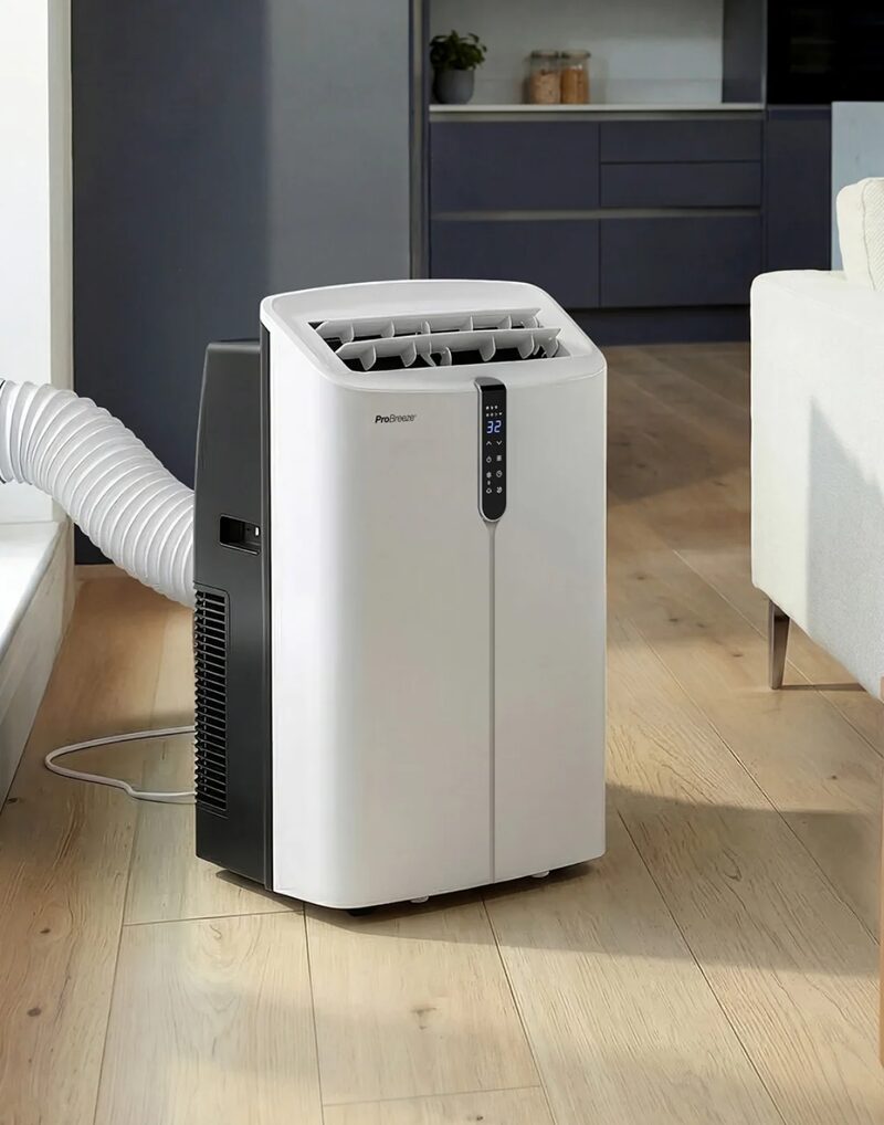 A white and black Pro Breeze portable air conditioner with an exhaust hose standing on a wooden floor in a modern living room