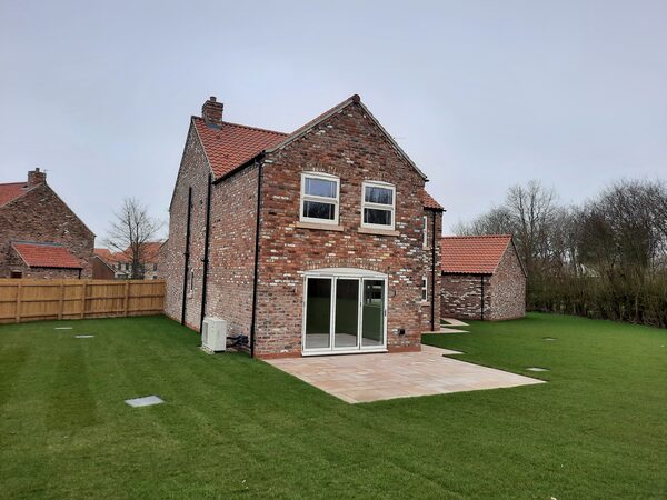 A new brick detached house with a heat pump unit installed on the rear wall beside the patio doors