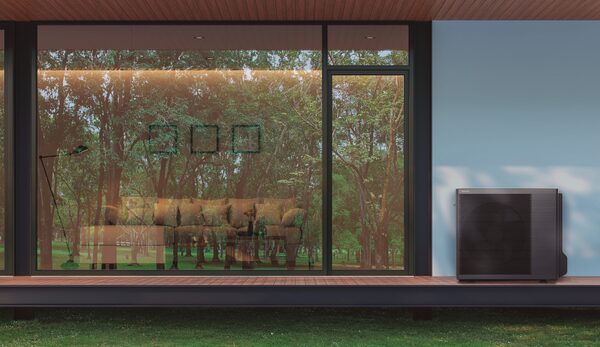 A Panasonic air source heat pump outdoor unit mounted on the wall of a modern house beside large glass windows