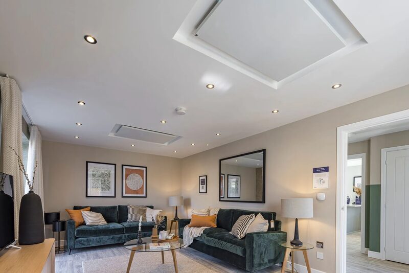 A modern living room with green velvet sofas and a ceiling-mounted ventilation or heating unit recessed into the ceiling